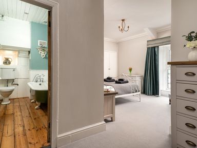 A bedroom with a bed towels and flowers next to a bathroom with a bathtub and wooden floor at Fron Dderw Bala
