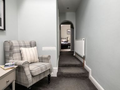 A hallway with a grey plaid armchair and a side table leading to a bedroom at Fron Dderw in Bala