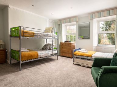 A bedroom with bunk beds a single bed a wooden dresser and a green armchair at Fron Dderw in Bala