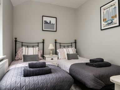 A bedroom with two single beds grey quilted bedspreads towels on beds a nightstand with a lamp and framed pictures on walls at Fron Dderw in Bala