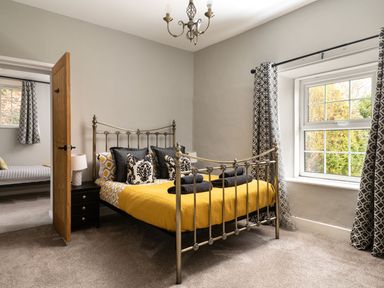 A bedroom with a metal bed frame yellow bedding and patterned curtains at Fron Dderw in Bala