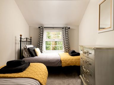 A bedroom with two beds with yellow quilts a window between them and a dresser with a mirror on the wall at Fron Dderw in Bala