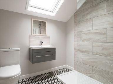 A bathroom with a toilet a wall-mounted sink with mirror a tiled shower area and a patterned floor at Fron Dderw in Bala