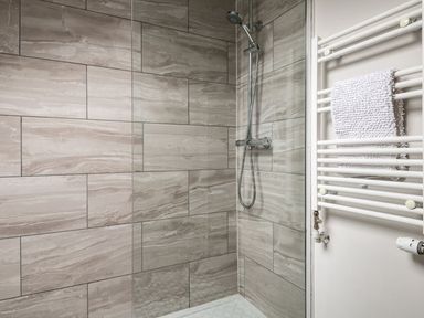 A shower area with tiled walls and a mounted handheld showerhead and a white towel on a heated rail at Fron Dderw in Bala