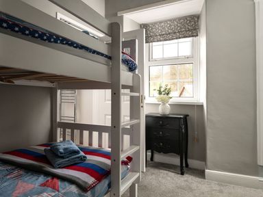 A bedroom with a white bunk bed and a black chest of drawers with a vase on top at Fron Dderw in Bala