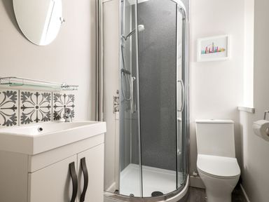 A bathroom with a shower enclosure a toilet a sink with cabinet and a round mirror above at Fron Dderw Bala