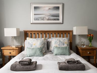 A bedroom with a wooden double bed with pillows and folded towels on a white bedspread with bedside tables holding lamps and flowers at Fron Dderw in Bala