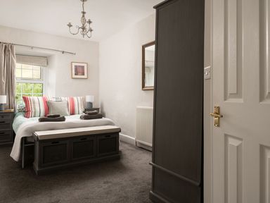 A bedroom with a bed with striped pillows two bedside tables with lamps a bench at the foot of the bed a wardrobe and a window at Fron Dderw in Bala