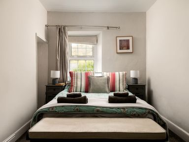 A bedroom with a double bed two bedside tables with lamps a window with curtains and a bench at Fron Dderw in Bala