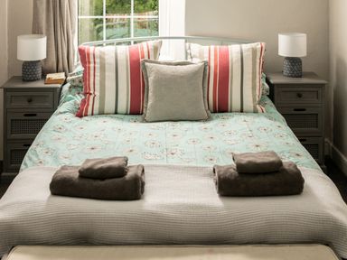 A bedroom with a bed with striped and plain pillows bedside tables with lamps and folded towels at Fron Dderw in Bala