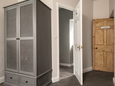 A room with a gray wardrobe two doors and two drawers an open white door leading to a hallway and a closed wooden door with a nameplate at Fron Dderw in Bala
