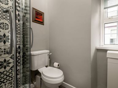 A bathroom with a shower enclosure with patterned tiles a toilet and a window at Fron Dderw in Bala