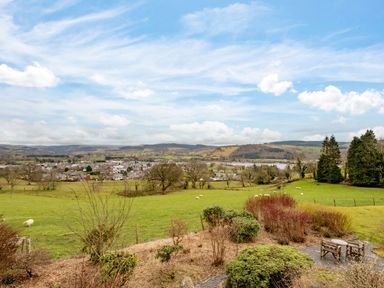 A garden with shrubs and a seating area overlooking a field with sheep and a town in the background at Fron Dderw Bala