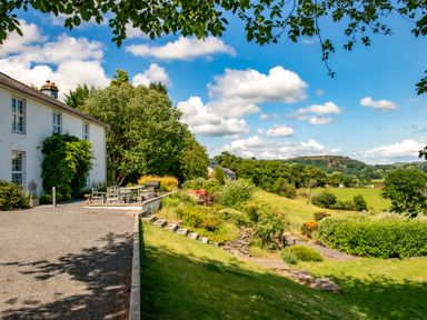 A house with an outdoor dining table and chairs next to a garden and fields at Fron Dderw in Bala