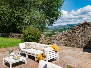 An outdoor patio area with white cushioned seating a low wooden table and a stone wall with a wooden gate at Fron Dderw in Bala