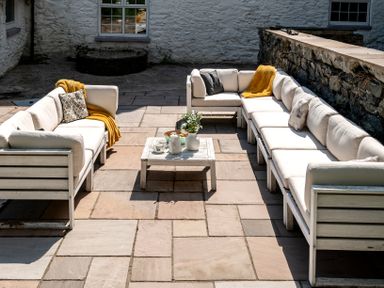 An outdoor patio with white cushioned sofas around a coffee table with a vase and teapot at Fron Dderw Bala