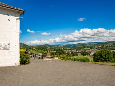 An outdoor seating area with tables and chairs next to a white building overlooking a town and hills at Fron Dderw in Bala
