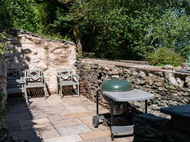 An outdoor patio area with three chairs and a barbecue grill next to stone walls at Fron Dderw in Bala