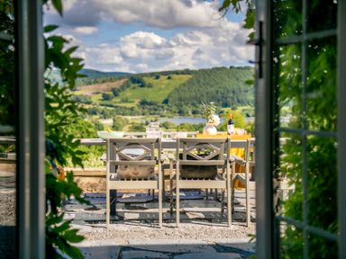 An outdoor dining table with chairs and tableware on a terrace overlooking hills and a lake at Fron Dderw Bala