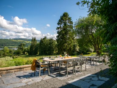 An outdoor dining area with a table and chairs on a stone patio overlooking a grassy landscape with trees at Fron Dderw Bala