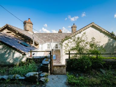 The rear view of a stone cottage with three chimneys and a small garden area with plants at Fron Dderw in Bala