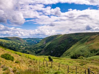A valley with green hills and a fence line under a partly cloudy sky at Fron Dderw in Bala