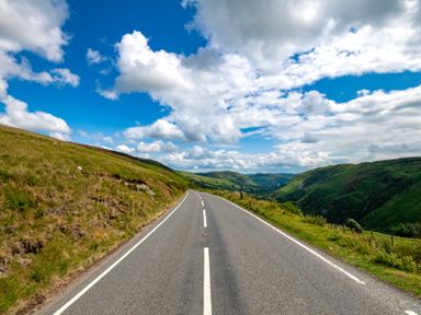 A paved road running through grassy hills under a partly cloudy sky at Fron Dderw in Bala