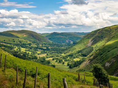 A valley with green fields trees and hills under a partly cloudy sky at Fron Dderw in Bala