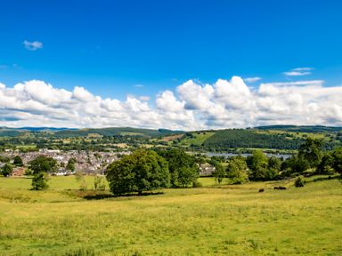 A rural landscape with green fields trees a small town and hills under a blue sky at Fron Dderw in Bala