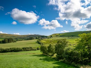 A landscape with green fields trees and hills under a blue sky with clouds at Fron Dderw in Bala