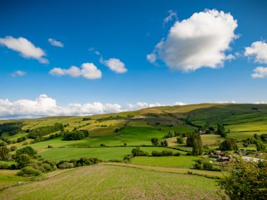 A rural landscape with green fields hills scattered trees and clouds in the sky at Fron Dderw in Bala