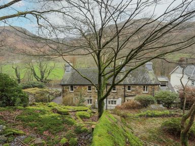 A mossy garden with a leafless tree and stone cottages in a rural hilly landscape at Glyn Awel in Nant Gwynant near Beddgelert