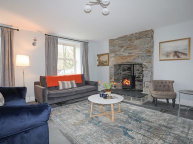 A living room with a stone fireplace a round white coffee table and sofas at Glyn Awel in Nant Gwynant near Beddgelert