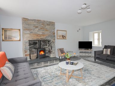 A living room with a stone fireplace wood stove two sofas a round white coffee table and a television at Glyn Awel in Nant Gwynant near Beddgelert