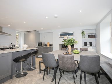 A kitchen and dining area with a table and chairs a kitchen island with bar stools and kitchen appliances at Glyn Awel in Nant Gwynant near Beddgelert