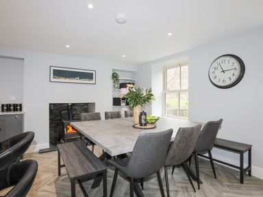 A dining room with a table chairs benches a clock and a fireplace at Glyn Awel in Nant Gwynant near Beddgelert