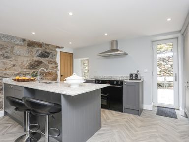 A kitchen with a stone wall an island with stools and a stove with a hood at Glyn Awel Nant Gwynant near Beddgelert