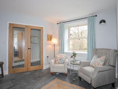 A sitting area with two armchairs a small round table with flowers curtains and double wooden doors at Glyn Awel Nant Gwynant near Beddgelert