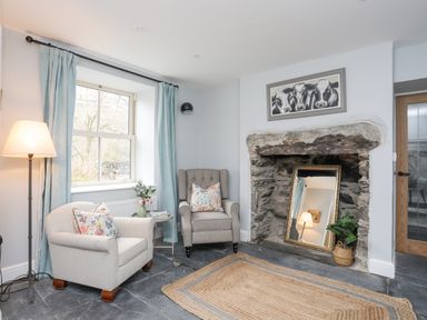 A sitting area with two armchairs a floor lamp a mirror inside a stone fireplace and a window with blue curtains at Glyn Awel in Nant Gwynant near Beddgelert