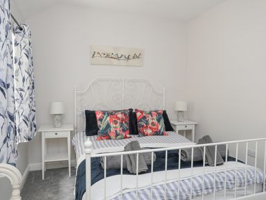 A bedroom with a white metal bed frame side tables with lamps and patterned curtains at Glyn Awel in Nant Gwynant near Beddgelert