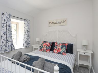 A bedroom with a white metal bed frame floral pillows bedside tables with lamps and patterned curtains at Glyn Awel in Nant Gwynant near Beddgelert
