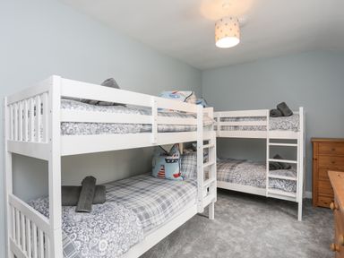 A bedroom with two white bunk beds a wooden chest of drawers and a ceiling lamp at Glyn Awel Nant Gwynant near Beddgelert