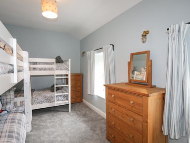 A bedroom with bunk beds a chest of drawers a mirror and striped curtains at Glyn Awel Nant Gwynant near Beddgelert