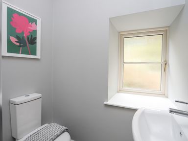 A bathroom with a toilet, sink, window, and artwork on the wall at Glyn Awel in Nant Gwynant near Beddgelert