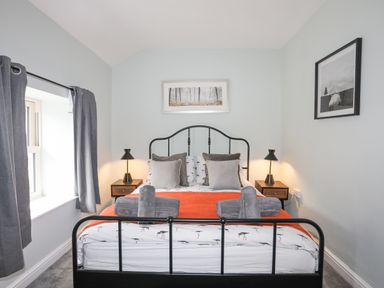 A bedroom with a black metal bed frame orange blanket gray pillows bedside tables lamps and two framed pictures on the walls at Glyn Awel in Nant Gwynant near Beddgelert