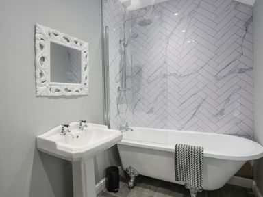 A bathroom with a clawfoot bathtub shower combination and a pedestal sink with a decorative mirror on the wall at Glyn Awel in Nant Gwynant near Beddgelert