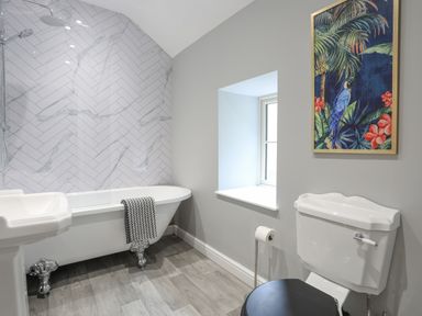 A bathroom with a clawfoot bathtub towel window toilet and framed artwork at Glyn Awel in Nant Gwynant near Beddgelert