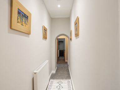 A hallway with framed pictures on the walls a radiator on the left and a rug on the floor at Glyn Awel in Nant Gwynant near Beddgelert