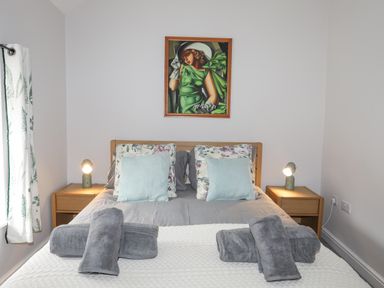 A bedroom with a bed with pillows and rolled towels bedside tables with lamps and a painting above the bed at Glyn Awel in Nant Gwynant near Beddgelert