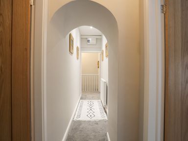 A hallway with an arch ceiling carpet on the floor and framed pictures on the walls at Glyn Awel in Nant Gwynant near Beddgelert
